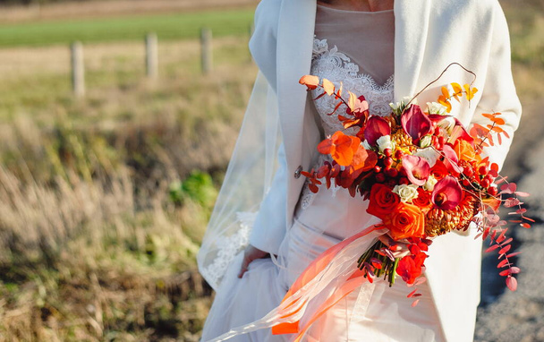Düğün için. Beyaz elbiseli kız doğa arka planında duruyor ve elinde bir buket kırmızı, beyaz çiçek tutuyor. Yaklaş. Renkli, modern sonbahar düğün buketi tutan gelin. Mesaj için yer. Boşluğu kopyala. - Fotoğraf, Görsel