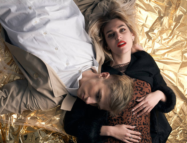 Stylish couple posing on a golden background from a foil lying. - Фото, зображення