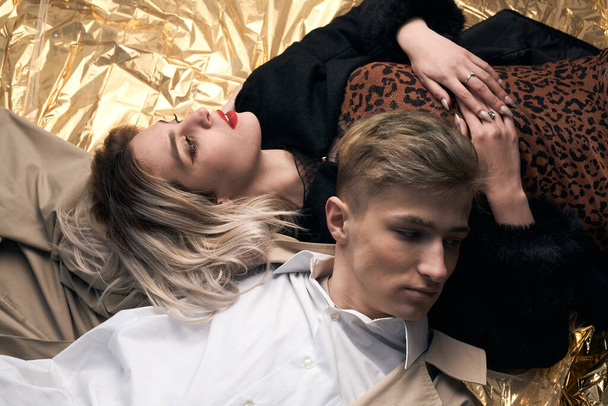 Stylish couple posing on a golden background from a foil lying. - Fotografie, Obrázek