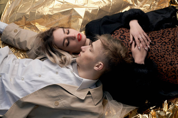 Stylish couple posing on a golden background from a foil lying. - Fotoğraf, Görsel