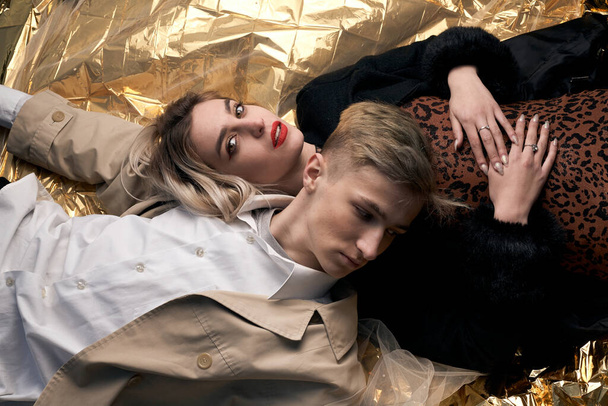 Stylish couple posing on a golden background from a foil lying. - Фото, изображение