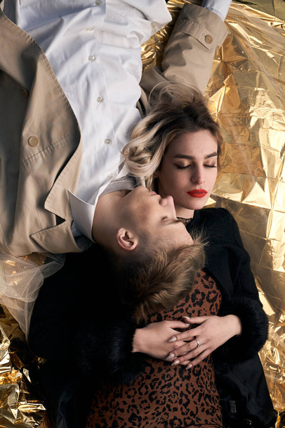 Casal elegante posando em um fundo dourado de uma folha metálica deitada
. - Foto, Imagem