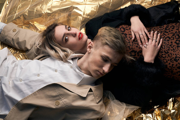 Stilvolles Paar posiert auf goldenem Hintergrund aus einer Folie liegend. - Foto, Bild