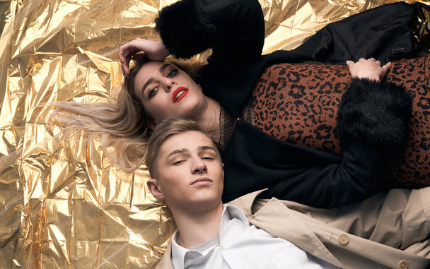 Stilvolles Paar posiert auf goldenem Hintergrund aus einer Folie liegend. - Foto, Bild