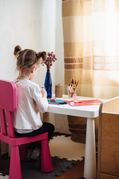 Девочка занимается творчеством дома, в детском саду. Ребенок вырезает бумагу. Детское искусство. Концепция ремесла. Сделано вручную. Раннее развитие ребенка. Что делать, чтобы изолировать ребенка - Фото, изображение