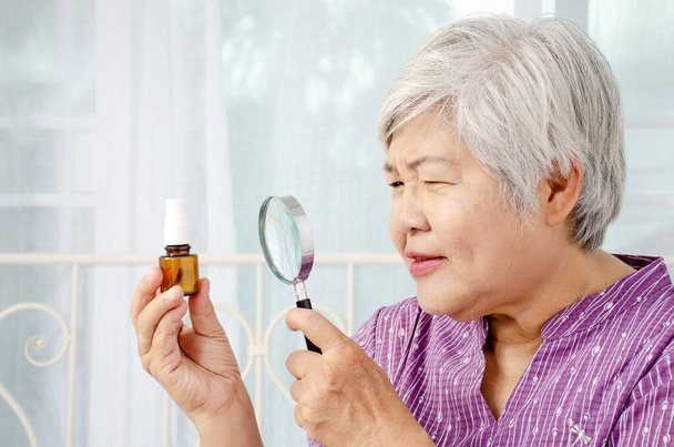 age, medicine, health care and people concept - Doubtful senior woman looking at medicine in his hand with Magnifying glass at home or hospital office - Photo, Image