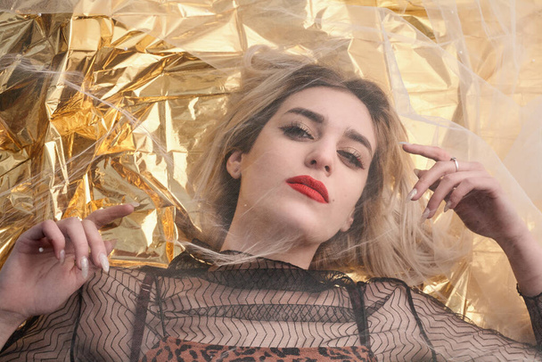 Beautiful girl with makeup on gold foil, under a tulle fabric. - Zdjęcie, obraz
