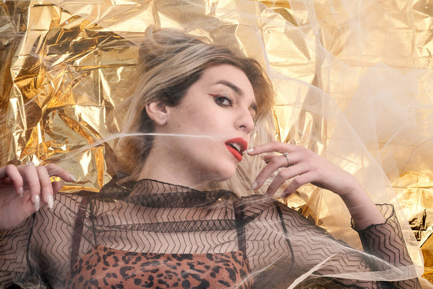 Beautiful girl with makeup on gold foil, under a tulle fabric. - Photo, Image