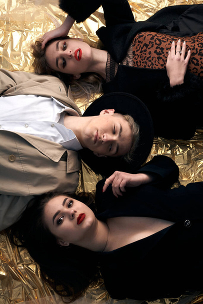 Stylish young people posing while lying on a gold background. - Foto, immagini
