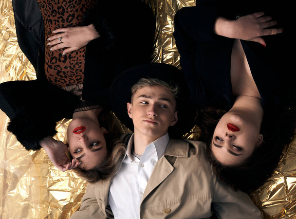 Stylish young people posing while lying on a gold background. - Zdjęcie, obraz