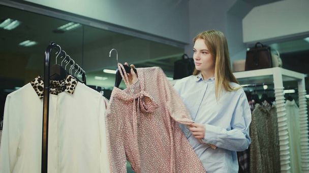 Cliente feminino atraente está escolhendo blusa no quarto de montagem
 - Foto, Imagem