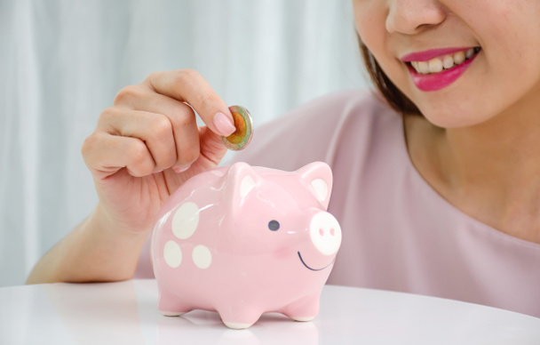Щаслива азіатська жінка вкладає грошову монету в свинарство для економії грошей багатства і фінансової концепції
. - Фото, зображення