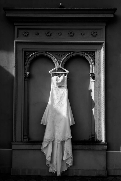 La robe de mariée de la mariée est suspendue à une arche en plâtre. Le soleil tombe sur la robe. Ombre. - Photo, image