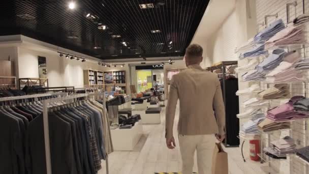 Tevreden klant na het winkelen met een tas in zijn handen verlaat de winkel van merkkleding. - Video