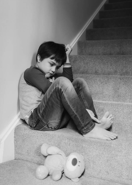 Triste menino asiático vestindo sentado na escada do tapete pela manhã, garoto solitário olhando dow com rosto triste não feliz para voltar para a escola, menino deprimido está sentado no canto de uma escada. Saúde mental
 - Foto, Imagem