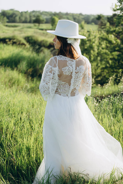 fashionable woman wearing fedora hat in white dress standing  in the field,  back view of - Fotó, kép