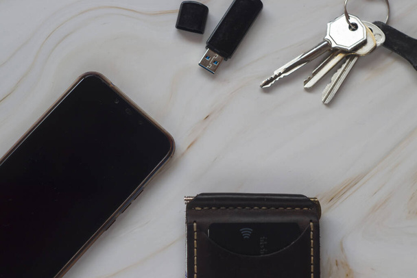 Nahkakortin haltija, avaimet, kännykkä ja muistitikku pöydällä. Toimiston tausta freelance, koulutus - Valokuva, kuva