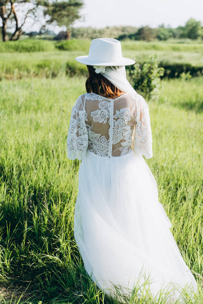 fashionable woman wearing fedora hat in white dress standing  in the field,  back view of - Photo, Image