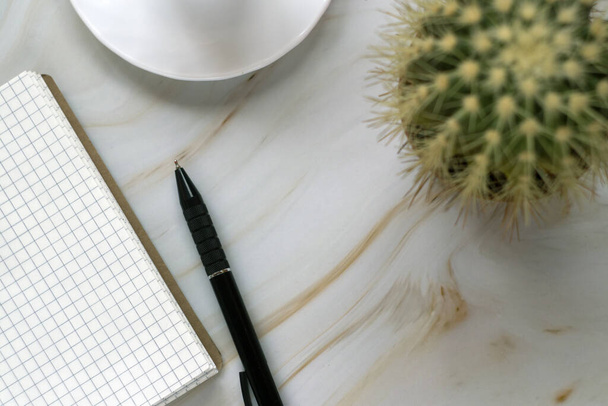 A white cup of espresso on the marble background with cactus, notepad and a pen - Photo, Image