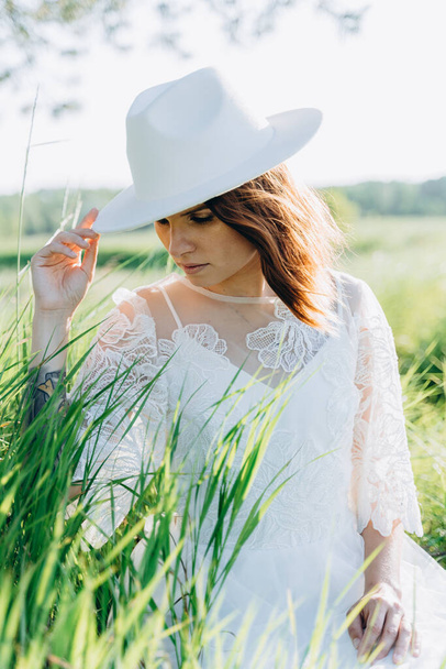 portrait of attractive woman wearing fedora hat sitting in summer meadow - Photo, Image