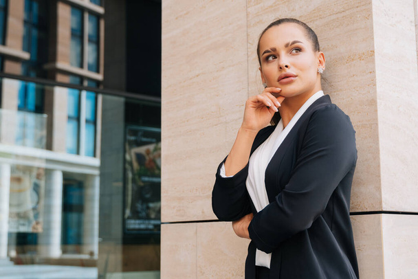 Elegant stylish lady is standing in a black formal suit leaning on the wall of a business center. girl closed her eyes in pleasure. - Foto, Bild