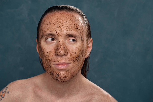 Hombre de ensueño con el pelo largo mojado en la máscara de café en su cara esperando los procedimientos de spa
. - Foto, Imagen