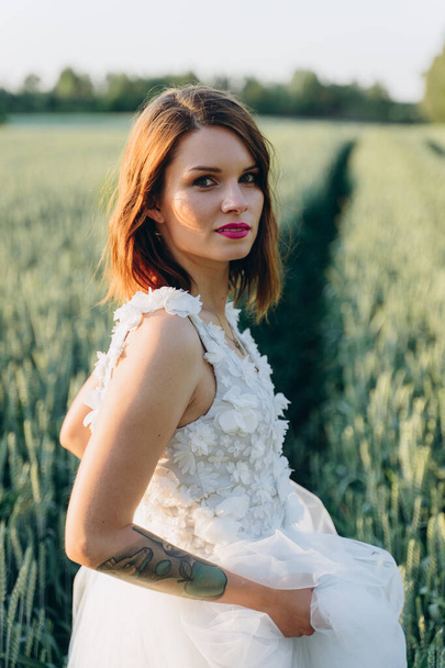 attractive young woman in long white dress standing in the field and looking at camera - Foto, Imagen