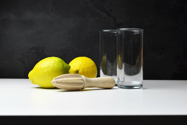 レモン柑橘系の果物で、木製の手スクイーザーと空のガラスが黒い背景の上に白いテーブルの上に - 写真・画像