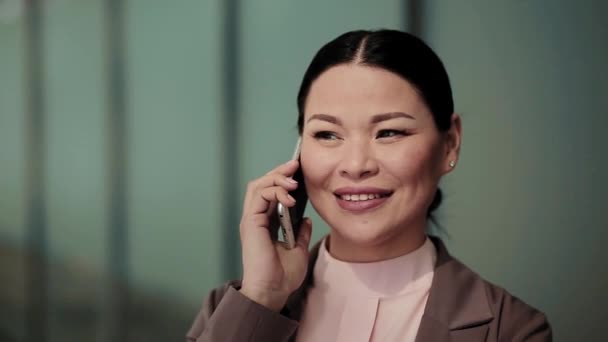 Asian business woman talking on the phone standing outdoors near office building. Beautiful woman having conversation on the phone with client. Business concept. Close up. Toned footage. Prores 422 - Materiał filmowy, wideo