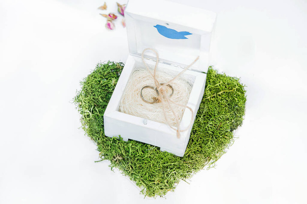 Платиновые обручальные кольца в деревянной коробке с птицей на белом фоне. Свадебные аксессуары ручной работы в деревенском стиле
 - Фото, изображение