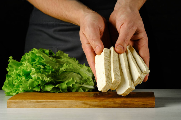 Queso de tofu picado en las manos de los cocineros en una tabla de madera
 - Foto, Imagen