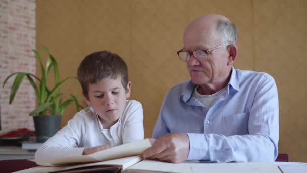stary dziadek w okularach na wzrok ze swoim sympatycznym wnukiem cieszyć się wspomnieniami przypominającymi oglądanie albumu rodzinnego zdjęcia - Materiał filmowy, wideo
