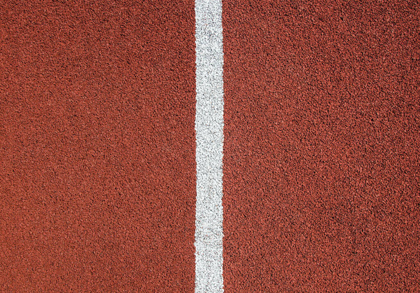 Red rubber running track texture close up. White divider line in the center. - Foto, Imagen