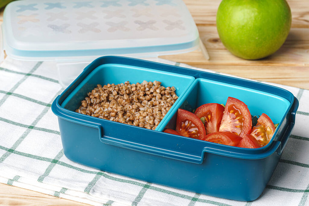 Blue lunch box with buckwheat and tomatoes - Фото, изображение