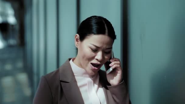Asian business woman walking and talking on the phone outdoors near office building. Beautiful woman having conversation on phone with client. Business concept. Cold tone. Toned footage. Prores 422 - Metraje, vídeo