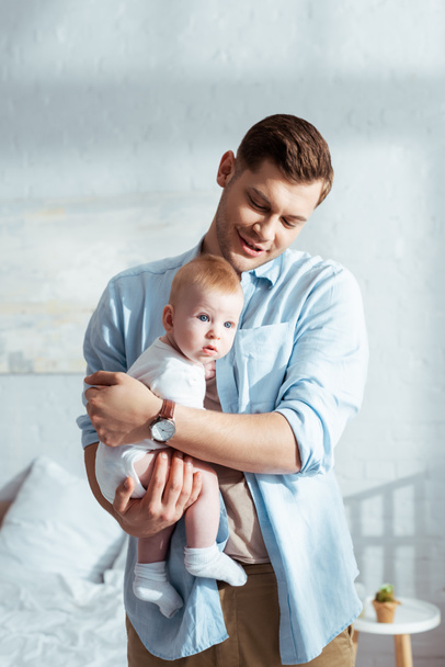 glücklicher Vater mit entzückendem Säugling auf Händen im Schlafzimmer - Foto, Bild