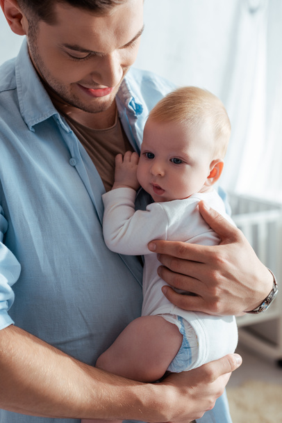 happy young father holding cute baby boy in romper on hands - Foto, Imagem
