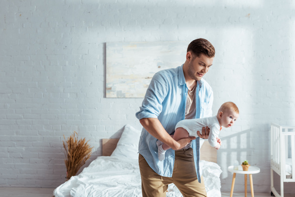 young father holding adorable little son in bedroom - Photo, Image