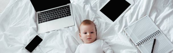 horizontal image of adorable baby boy lying near gadgets and notebook - Photo, Image