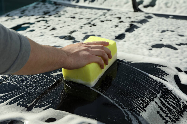 Ο άνθρωπος σκουπίζει το αυτοκίνητο με ένα σφουγγάρι. Καθαρίστε την έννοια του αυτοκινήτου - Φωτογραφία, εικόνα