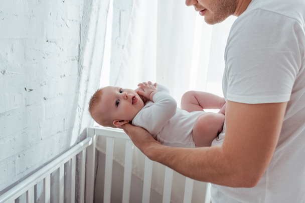vista recortada de padre sosteniendo adorable bebé niño sobre cuna
 - Foto, Imagen