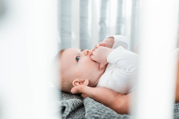 cropped view of man touching cute infant lying in baby cot, selective focus - Foto, afbeelding
