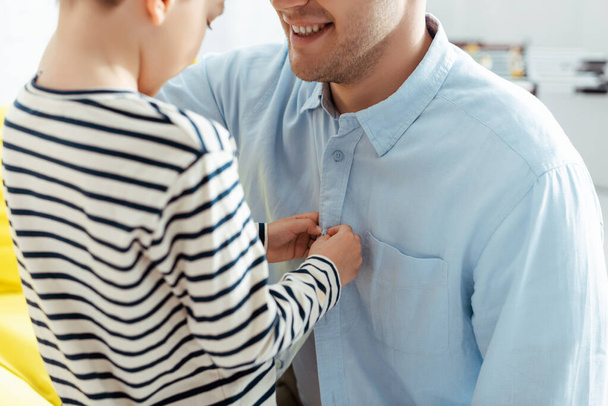 cropped view of boy buttoning shirt of smiling father - 写真・画像
