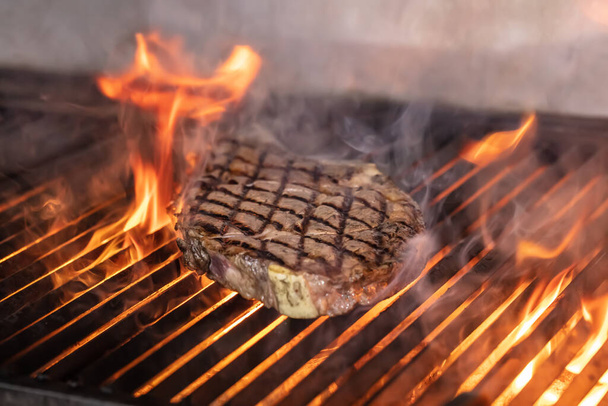 Beef steaks on the grill with flames. Grilling steaks on flaming grill and shot with selective focus. - Photo, Image