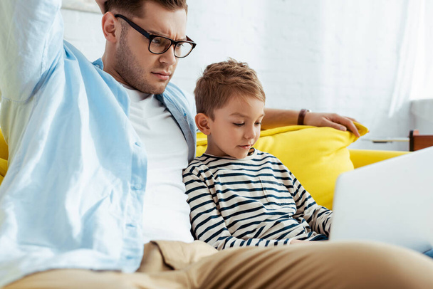thoughtful man with adorable son using laptop together - Foto, imagen