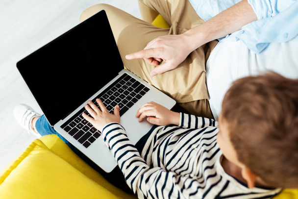 обрезанный вид отца указывая пальцем в то время как сын с помощью ноутбука с пустым экраном
 - Фото, изображение