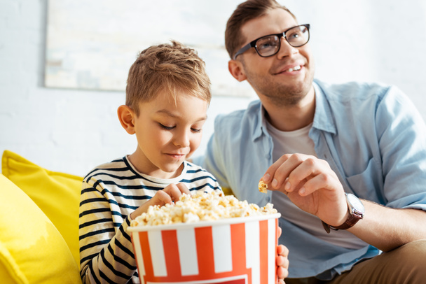selective focus of concentrated, excited man watching tv while eating popcorn with son - Φωτογραφία, εικόνα