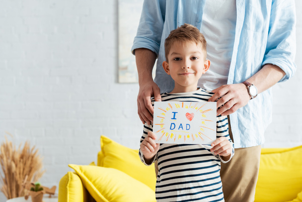 przycięty widok człowieka dotykającego ramion syna trzymającego ręcznie robione ojcowskie kartki okolicznościowe z literami i symbolem serca - Zdjęcie, obraz