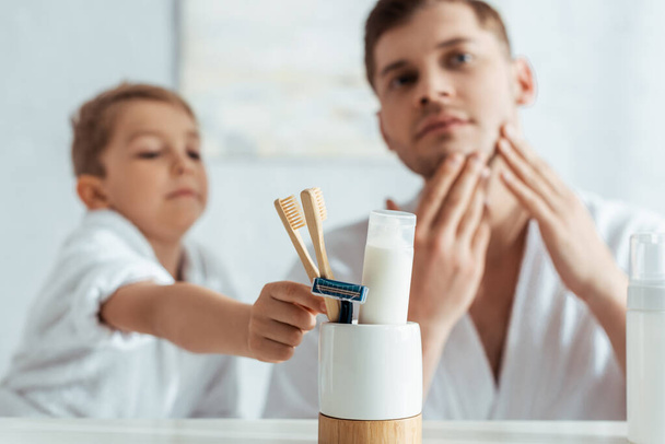 enfoque selectivo del hombre tocando la cara mientras que el hijo adorable toma cepillo de dientes
 - Foto, imagen