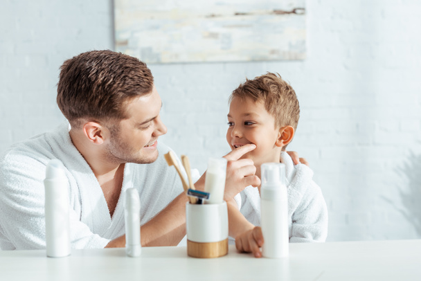 selective focus of happy father checking teeth of cute son near toiletries in bathroom - Photo, Image